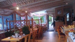 A restaurant with wooden tables and chairs, a tiled floor, and a view of the outdoors through large windows. - Gasthof Turm (Schoenwald)