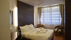 A hotel room with a large bed, a ceiling fan, a window with curtains, and a chair. - Ladybird Hotel (Shillong)