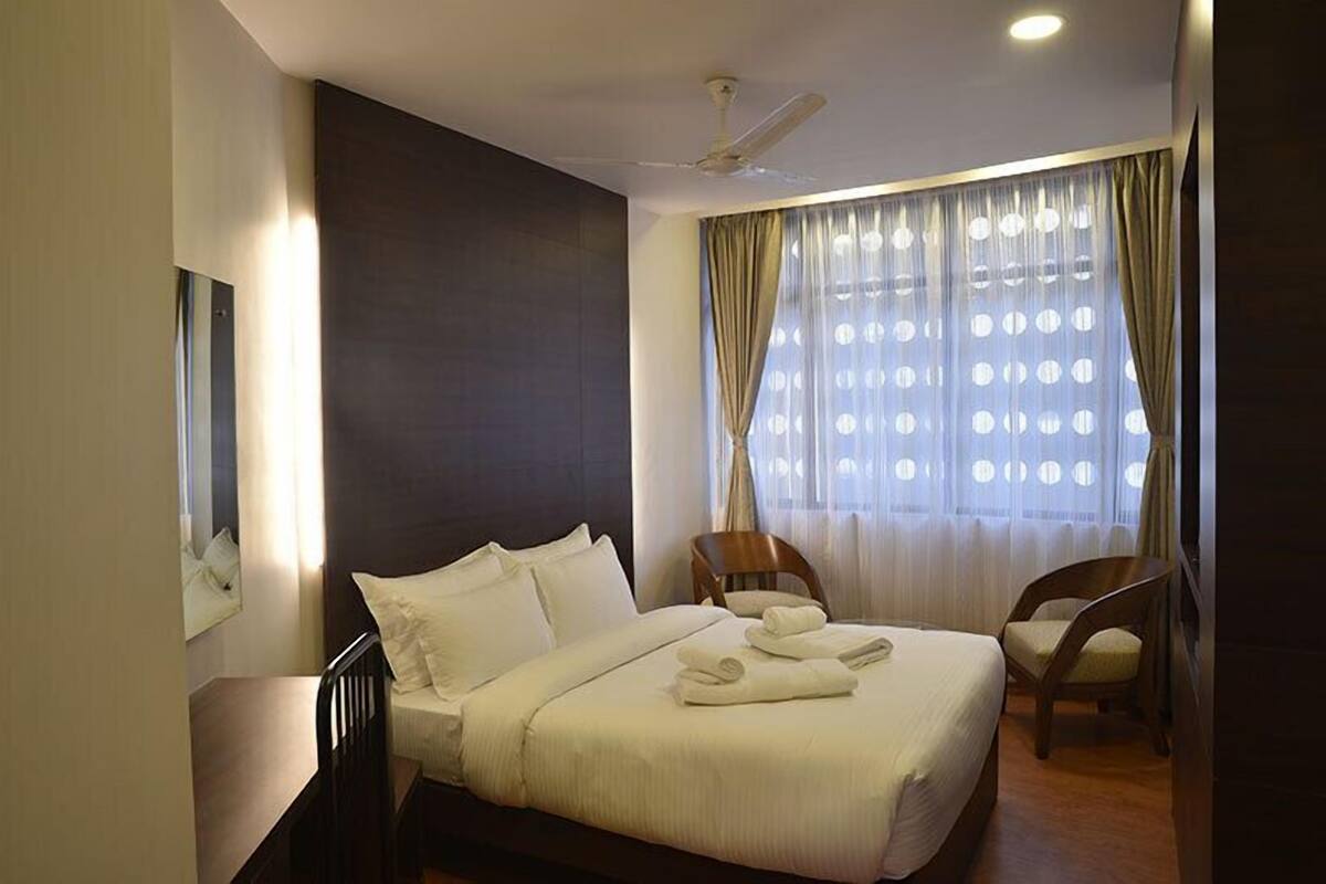 A hotel room with a large bed, a ceiling fan, a window with curtains, and a chair.