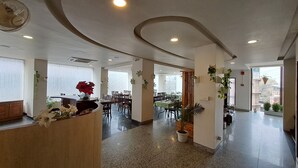 A hotel reception area with a curved ceiling, a reception desk, and several tables and chairs arranged for dining.