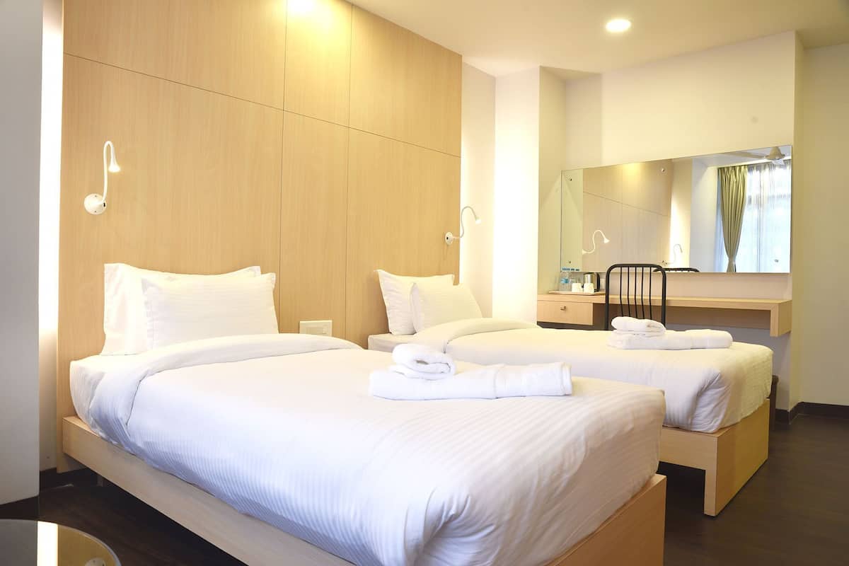 A hotel room with two beds, a wooden wardrobe, a desk, a chair, and a mirror.
