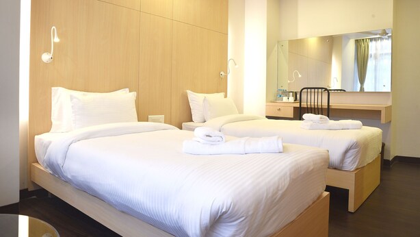 A hotel room with two beds, a wooden wardrobe, a desk with a mirror, and a bathroom.