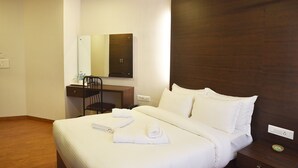 A hotel room with a bed, a desk with a chair, a mirror, and a nightstand.