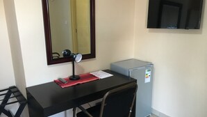 A small office space with a desk, chair, mirror, and a refrigerator. - Beautiful Gates Guest House (Palapye)