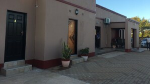 A building with numbered doors, potted plants, and a paved entrance area. - Beautiful Gates Guest House (Palapye)