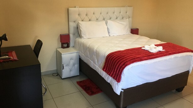 A neatly arranged hotel room with a bed, bedside tables, and a desk. - Beautiful Gates Guest House (Palapye)