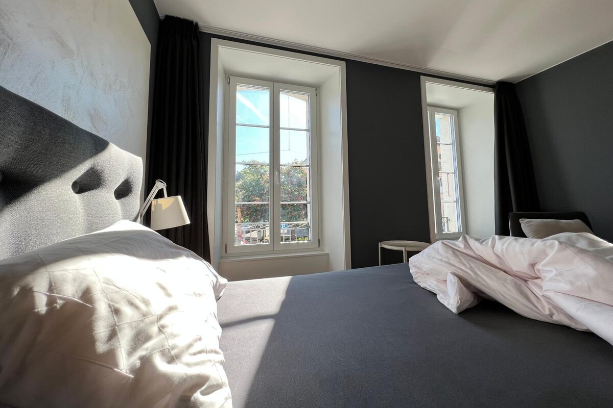 Een hotelkamer met een bed, een nachtkastje, een lamp en een raam met uitzicht.