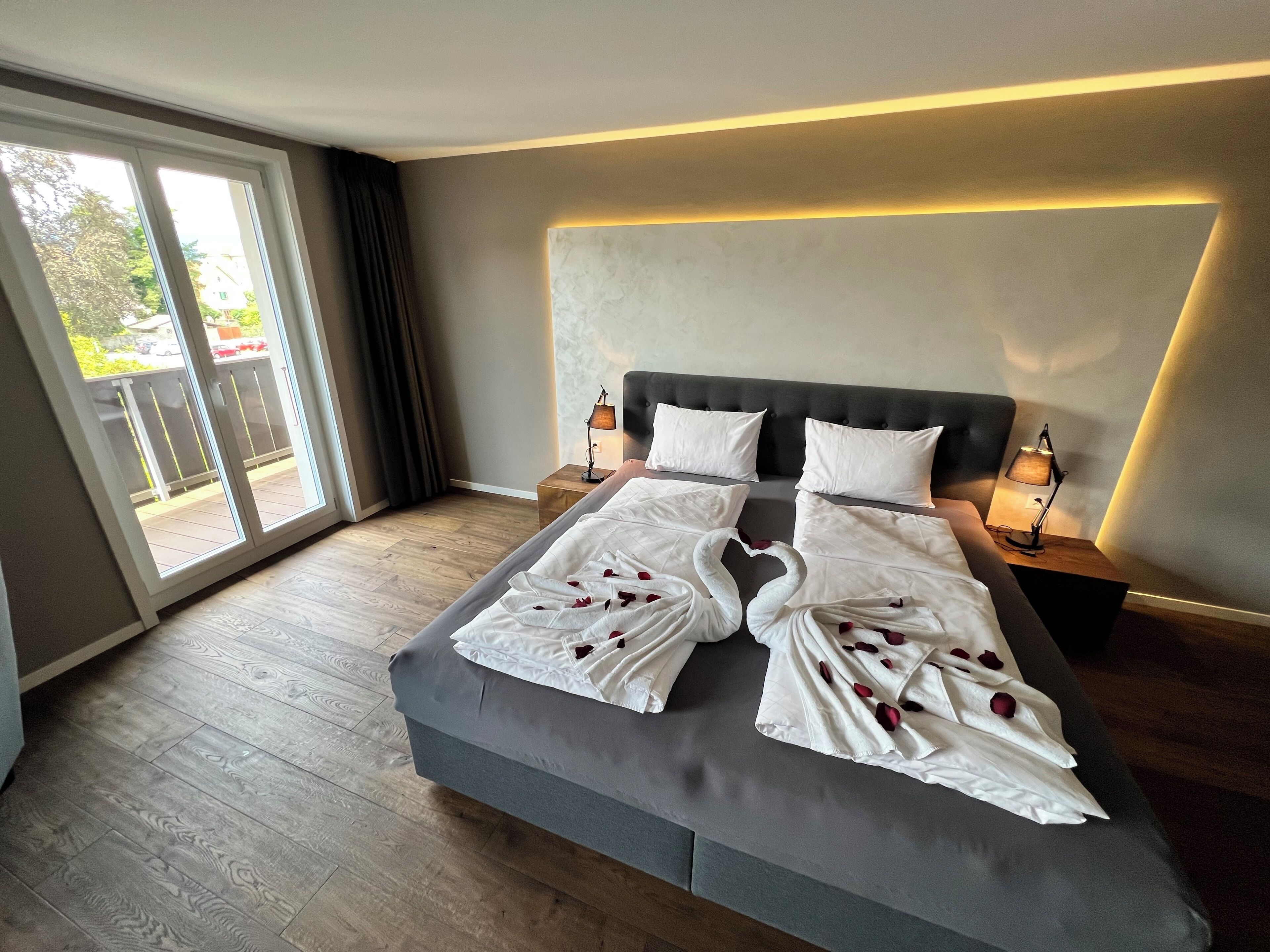 A hotel room with a large bed, two bedside tables with lamps, a sliding glass door to the balcony, and a modern headboard.