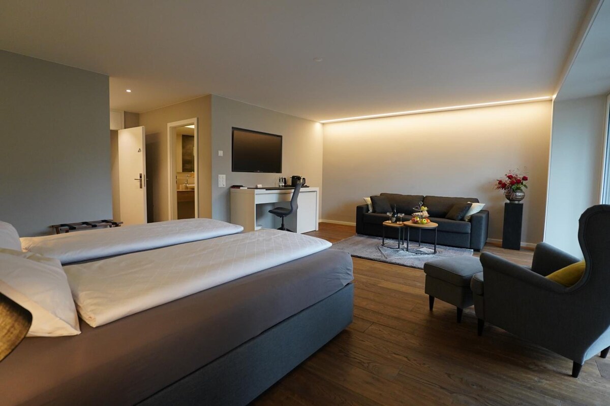 A hotel room with two beds, a desk, a sofa, and a chair.