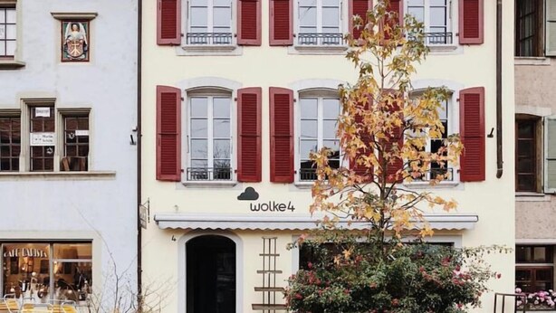 Ein Kopfsteinpflasterhof mit einem Gebäude, das rote Fensterläden und ein Schild mit der Aufschrift 'wolke4' zeigt.