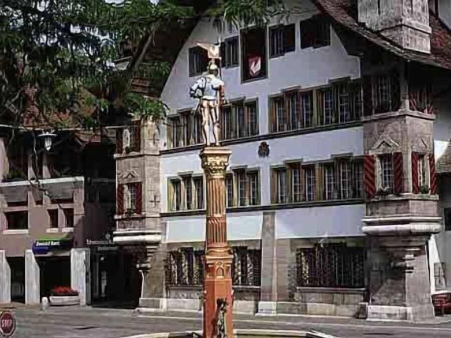 A building with a statue on a pedestal, multiple windows, and a stop sign.