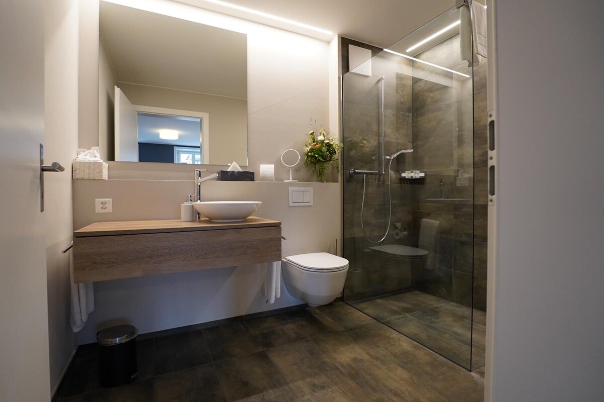 Ein modernes Badezimmer mit Duschkabine aus Glas, einem Holzkosmetikschrank und einer weißen Toilette.