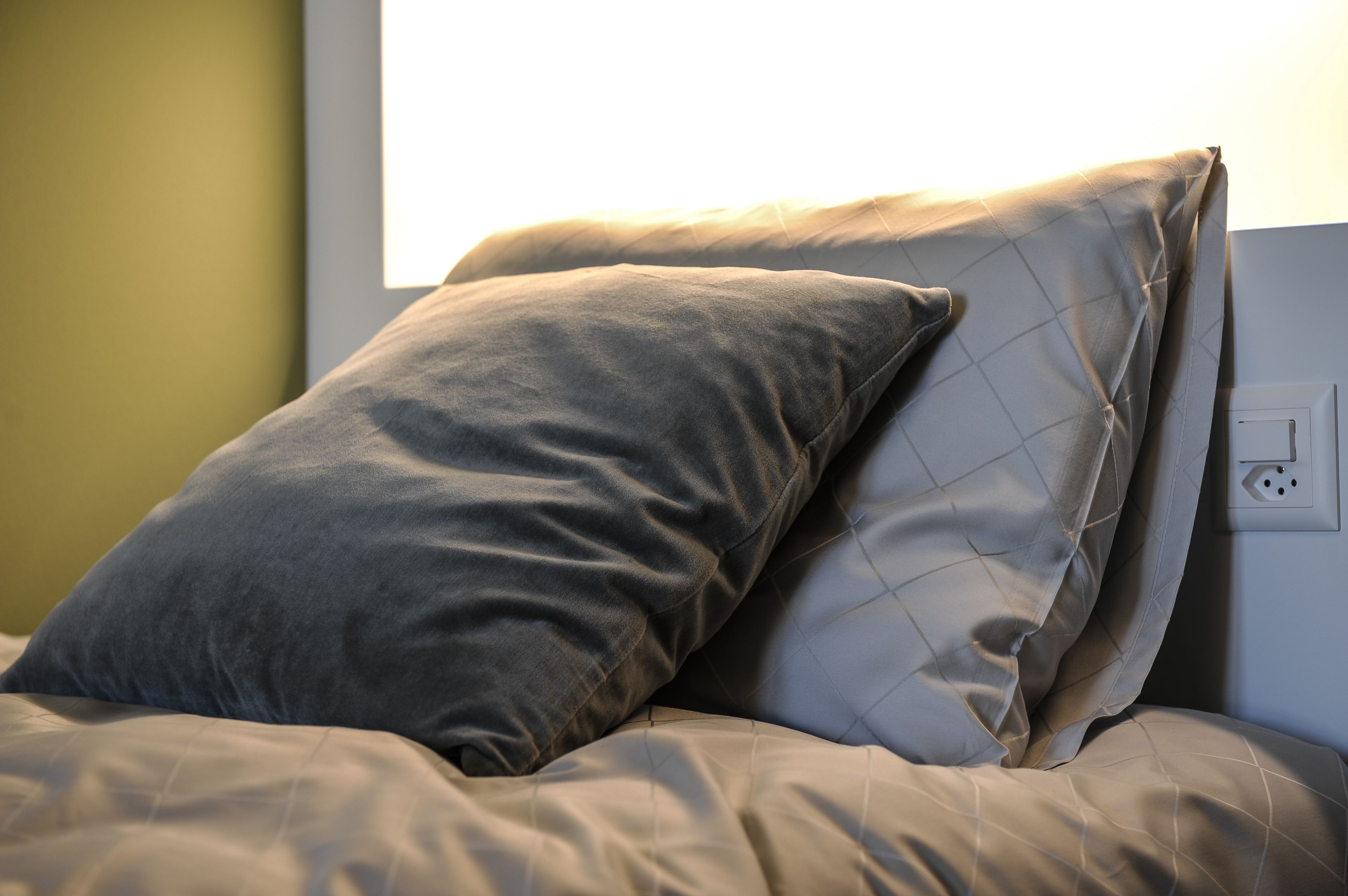 Una cama con dos almohadas y un enchufe en la pared.