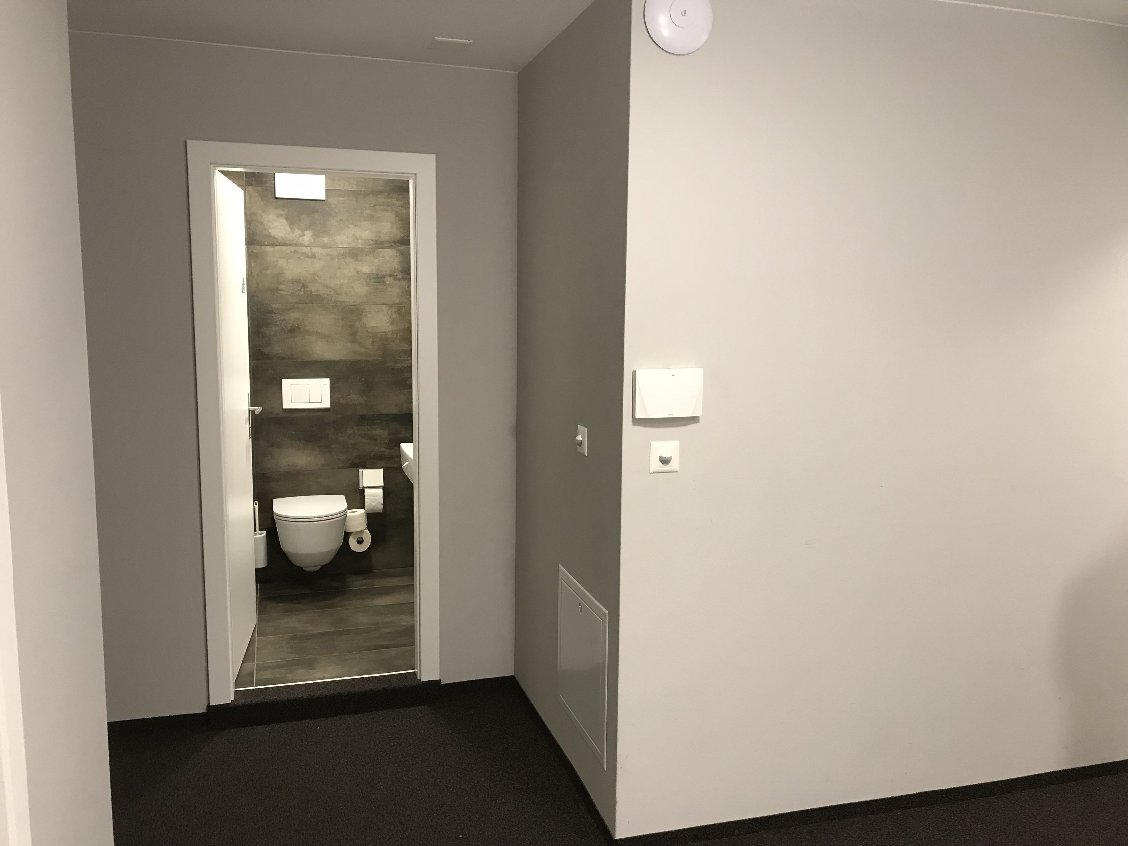 Pasillo que conduce a un baño con inodoro, lavamanos y dispensador de toallas.