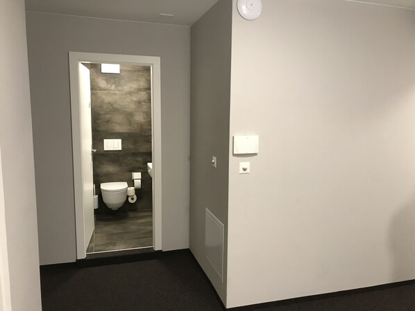 A hallway leading to a bathroom with a toilet, a sink, and a towel dispenser.