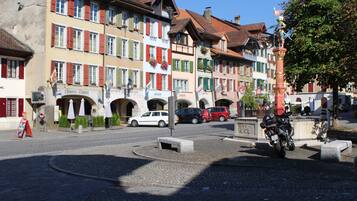 A cobblestone street with historic buildings, a roundabout, and a motorcycle parked near a statue.