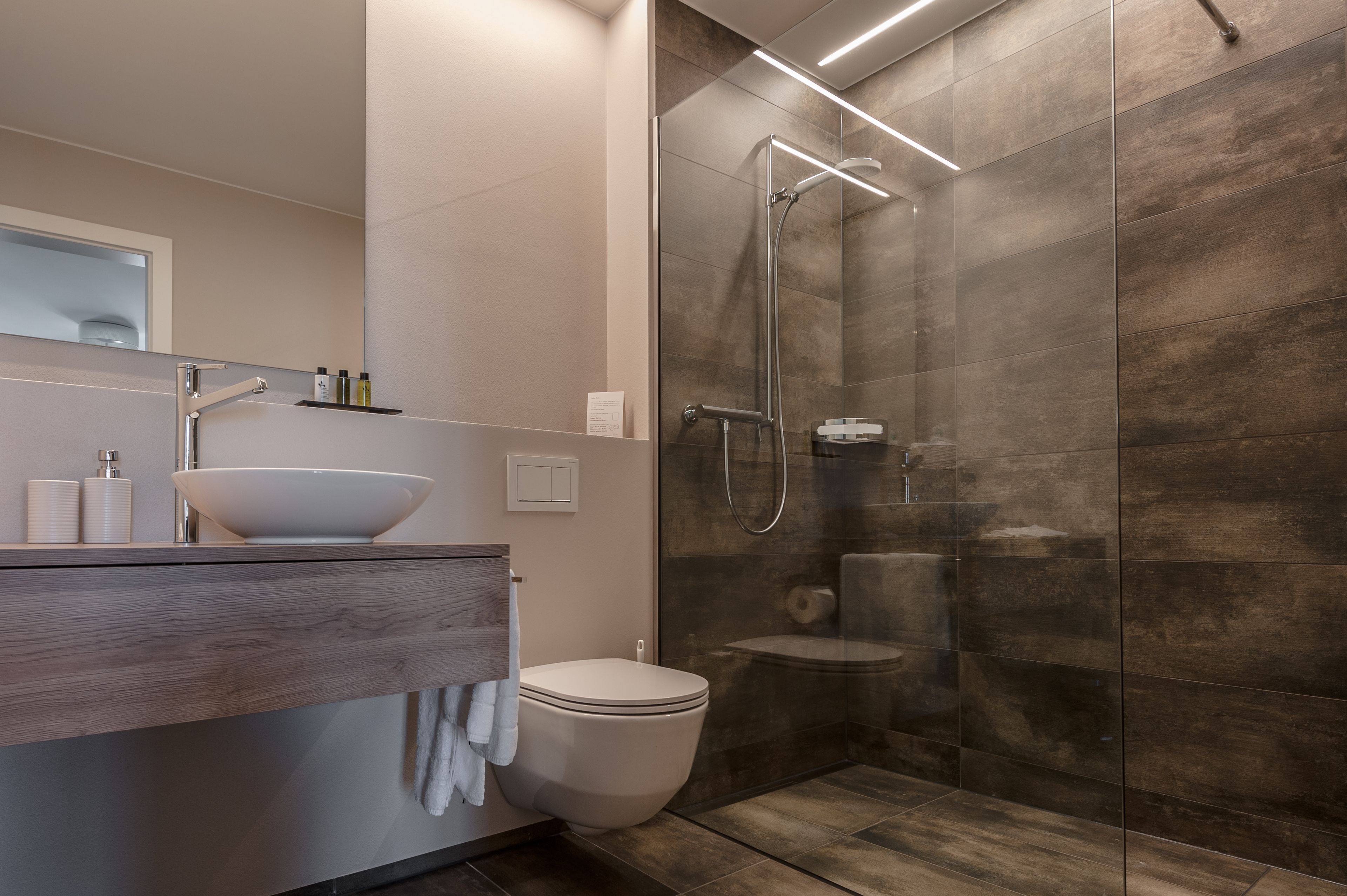 A modern bathroom with a glass-enclosed shower, a wooden vanity with a bowl sink, and a toilet.