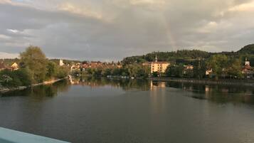 A calm river with buildings on the opposite bank, a rainbow in the sky, and a forested hill in the background.