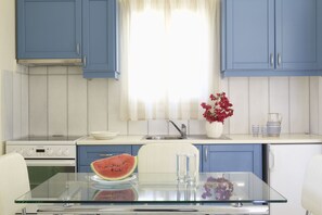 A kitchen with blue cabinets, a white countertop, a glass table, a watermelon slice, a vase with flowers, and a sink.