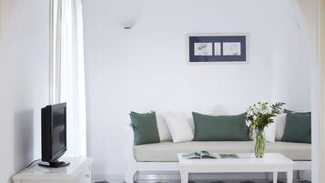 Un salon avec un canapé blanc, des coussins verts, une table basse blanche et un téléviseur posé sur un meuble blanc.