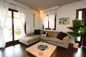 Ein Wohnzimmer mit einem Ecksofa, einem Couchtisch und einer großen Topfpflanze.