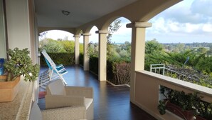 A covered outdoor area with a seating arrangement, including a sofa and chairs, overlooking a scenic landscape.