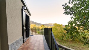 Un balcón con vista a un paisaje montañoso, un muro de piedra y una barandilla de metal.