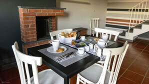 Comedor con chimenea de ladrillo, sillas blancas y una mesa lista para el desayuno.