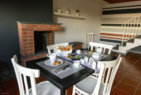 A dining area with a brick fireplace, white chairs, and a table set for breakfast.