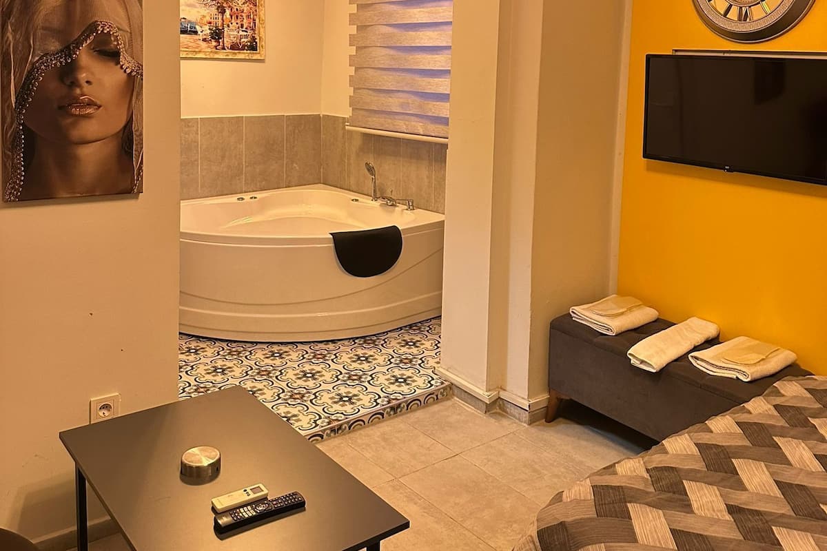 Un baño moderno con bañera, lavabo y espejo. Hay un reloj en la pared y un televisor sobre el lavabo.
