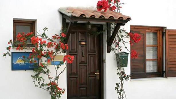 A traditional building with a dark wooden door, a tiled roof, and a small porch. There are potted plants and a sign on the wall.