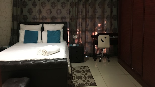 A hotel room with a bed, a desk, a chair, and a wardrobe. - Blomsbed Inn (Palapye)