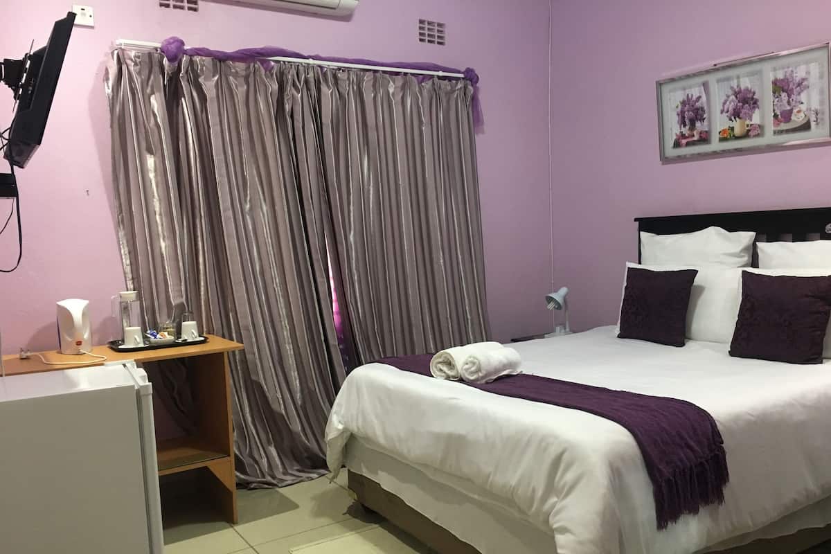 A neatly arranged bedroom with a bed, a bedside table, a lamp, and a window with curtains.