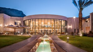 A modern hotel with a curved glass facade, outdoor seating area, and a central water feature.