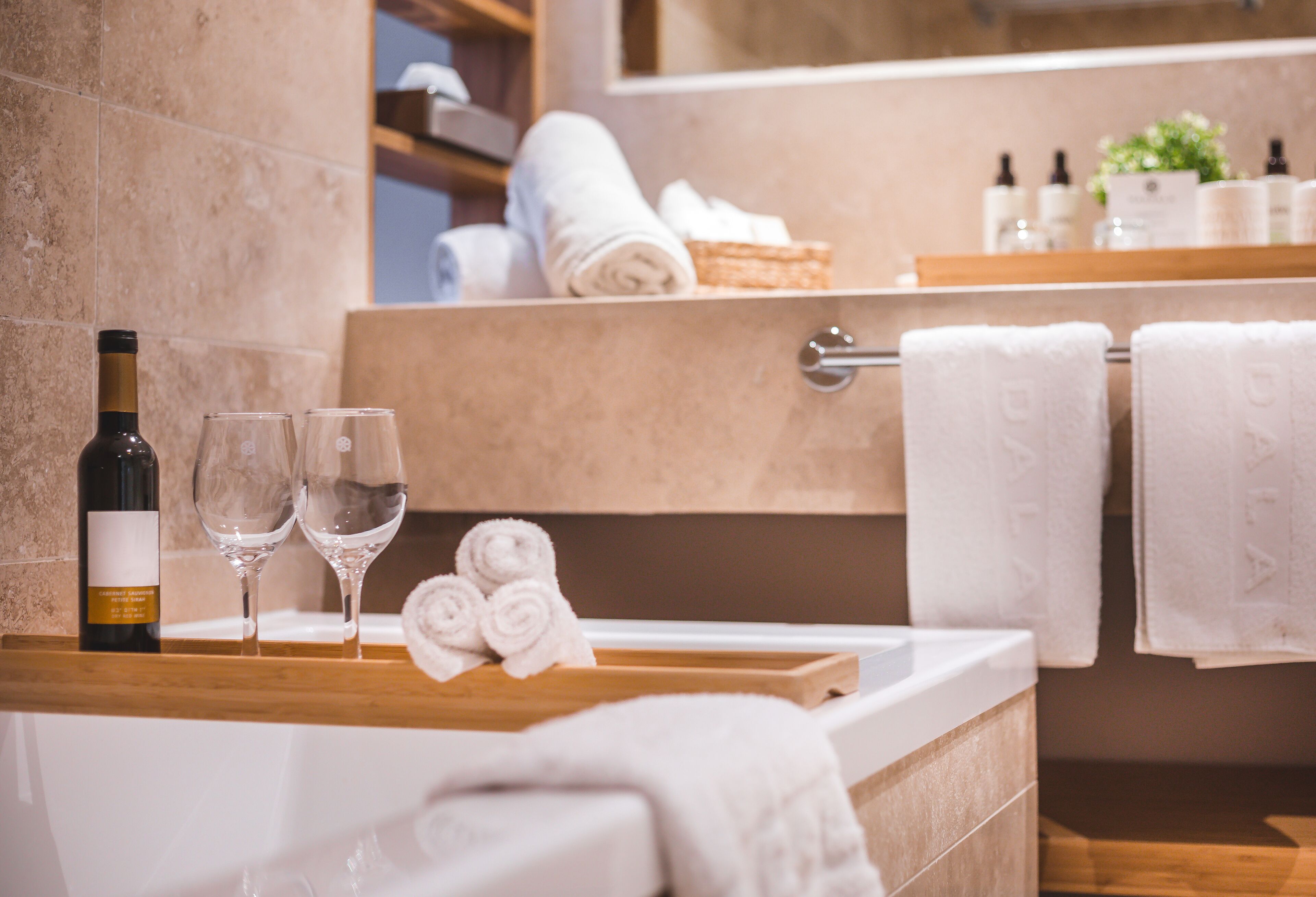 Une salle de bain avec une baignoire, deux verres à vin, une bouteille de vin et des serviettes soigneusement pliées.