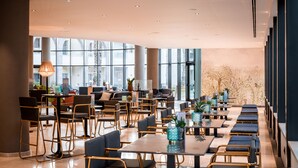 A spacious hotel lobby with high ceilings, large windows, and a modern interior design featuring a mix of seating arrangements and decorative elements.