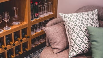 Una botellera con botellas y copas, un sofá acolchado con cojines estampados y un estante de madera.