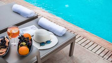 Mesa junto a la piscina con una bebida, frutas, un sombrero y toallas.