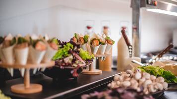 Una mesa de buffet con alimentos como champiñones y verduras, y una botella de vino al fondo.