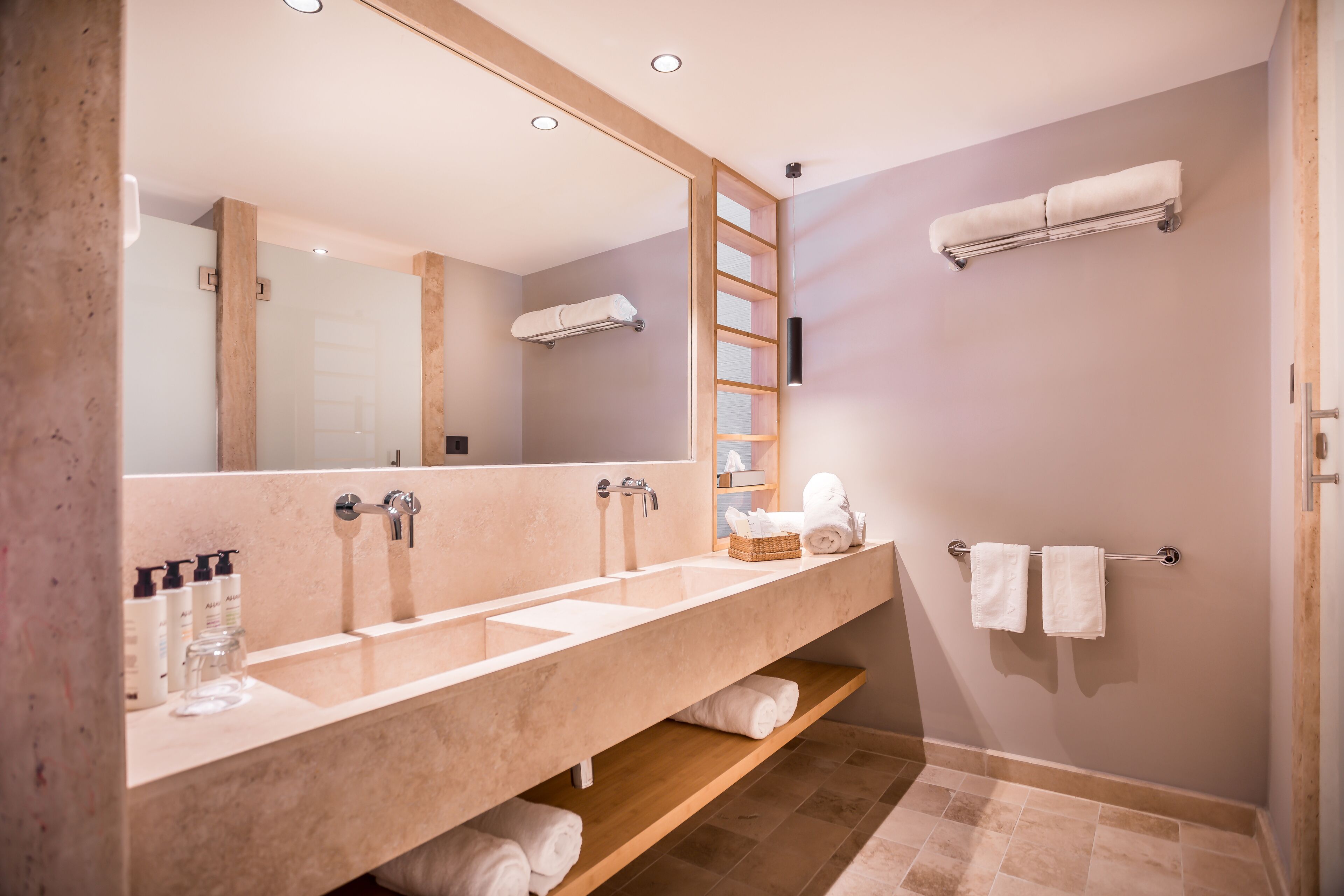 A modern bathroom with a large mirror, two sinks, a towel rack, and a wooden shelf.