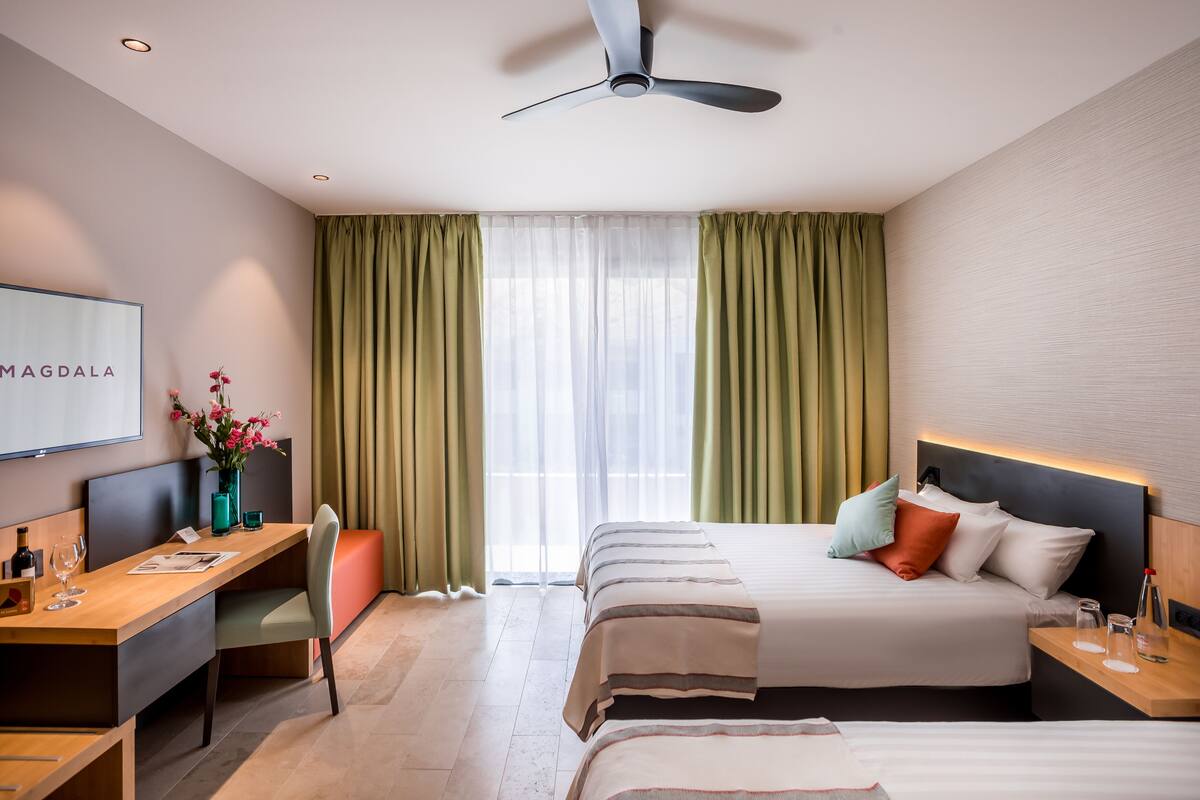 Ein Hotelzimmer mit Bett, Schreibtisch, Stuhl, Fernseher und Deckenventilator.