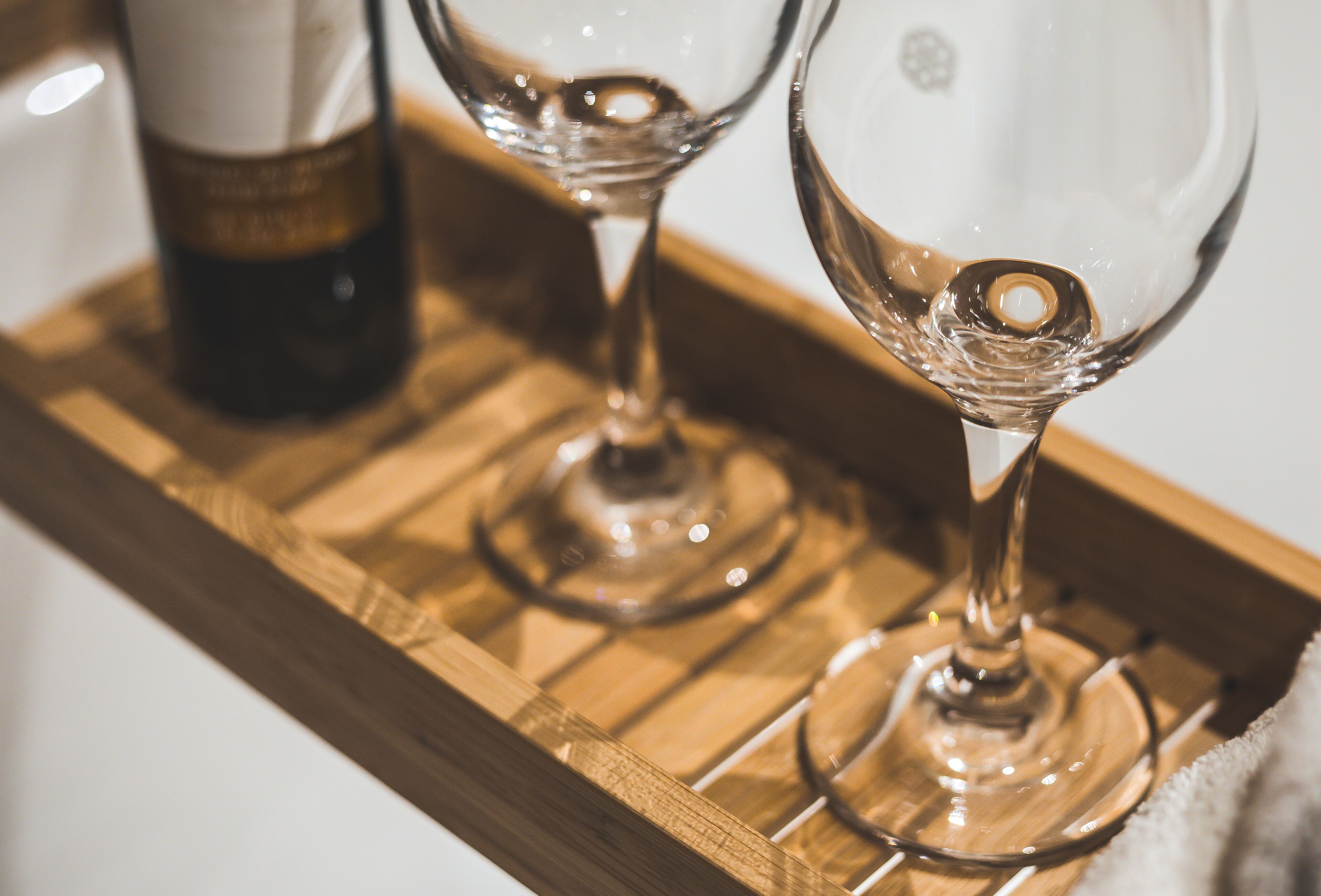 A wooden tray with two wine glasses and a bottle of wine.