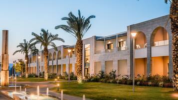 A modern building with arched windows and a well-maintained garden with palm trees and a fountain.