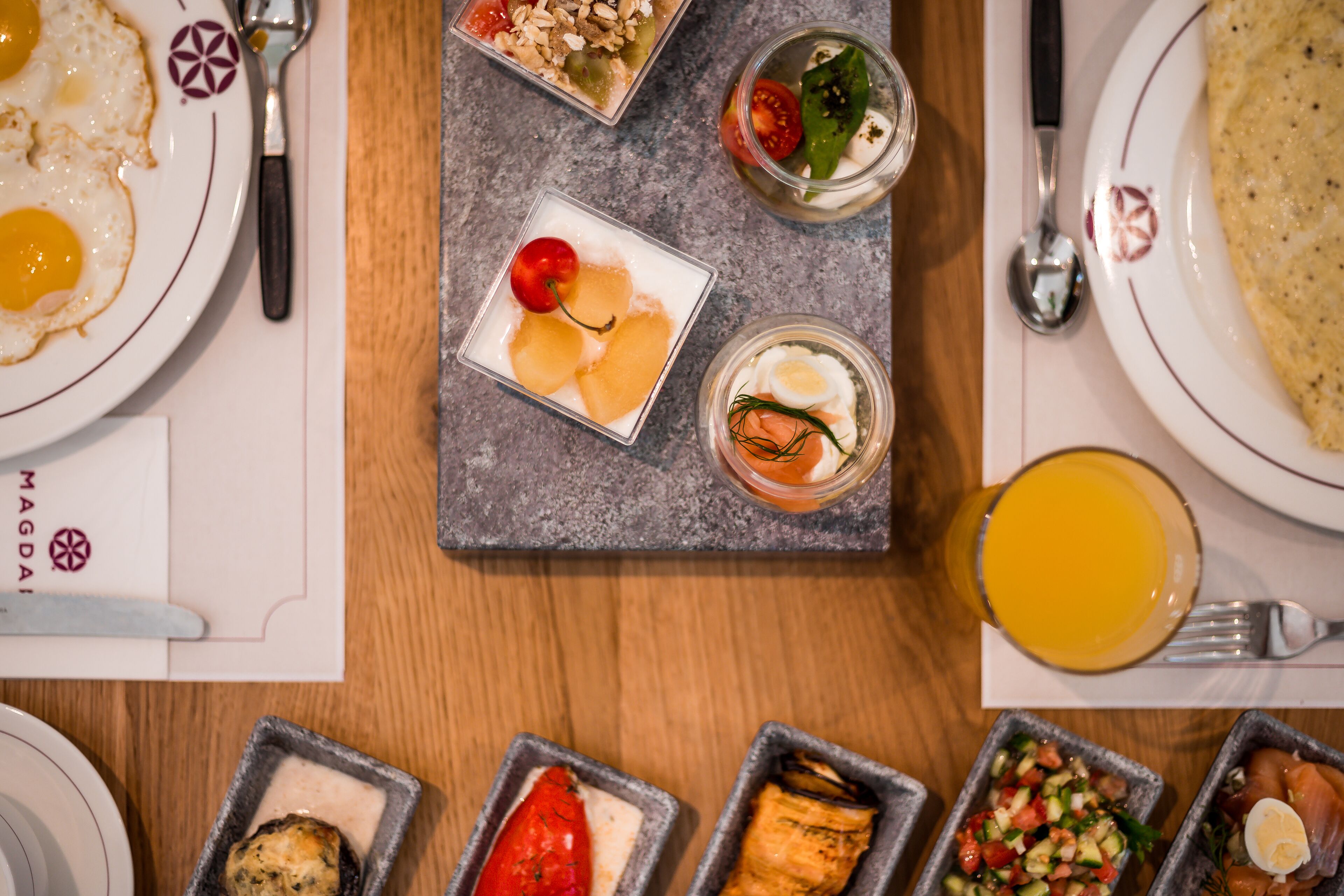 Diversos platos de desayuno en una mesa, como huevos, fruta y un vaso de zumo de naranja.