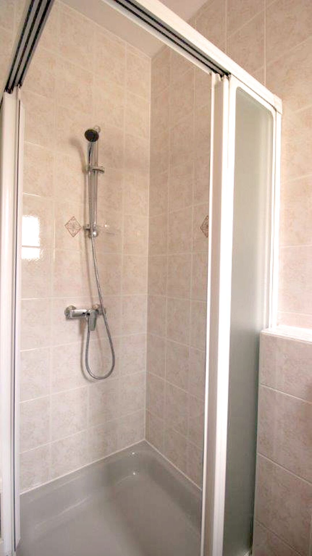 Une cabine de douche fermée par des parois en verre, dotée d’un pommeau de douche à main et d’un robinet mural.