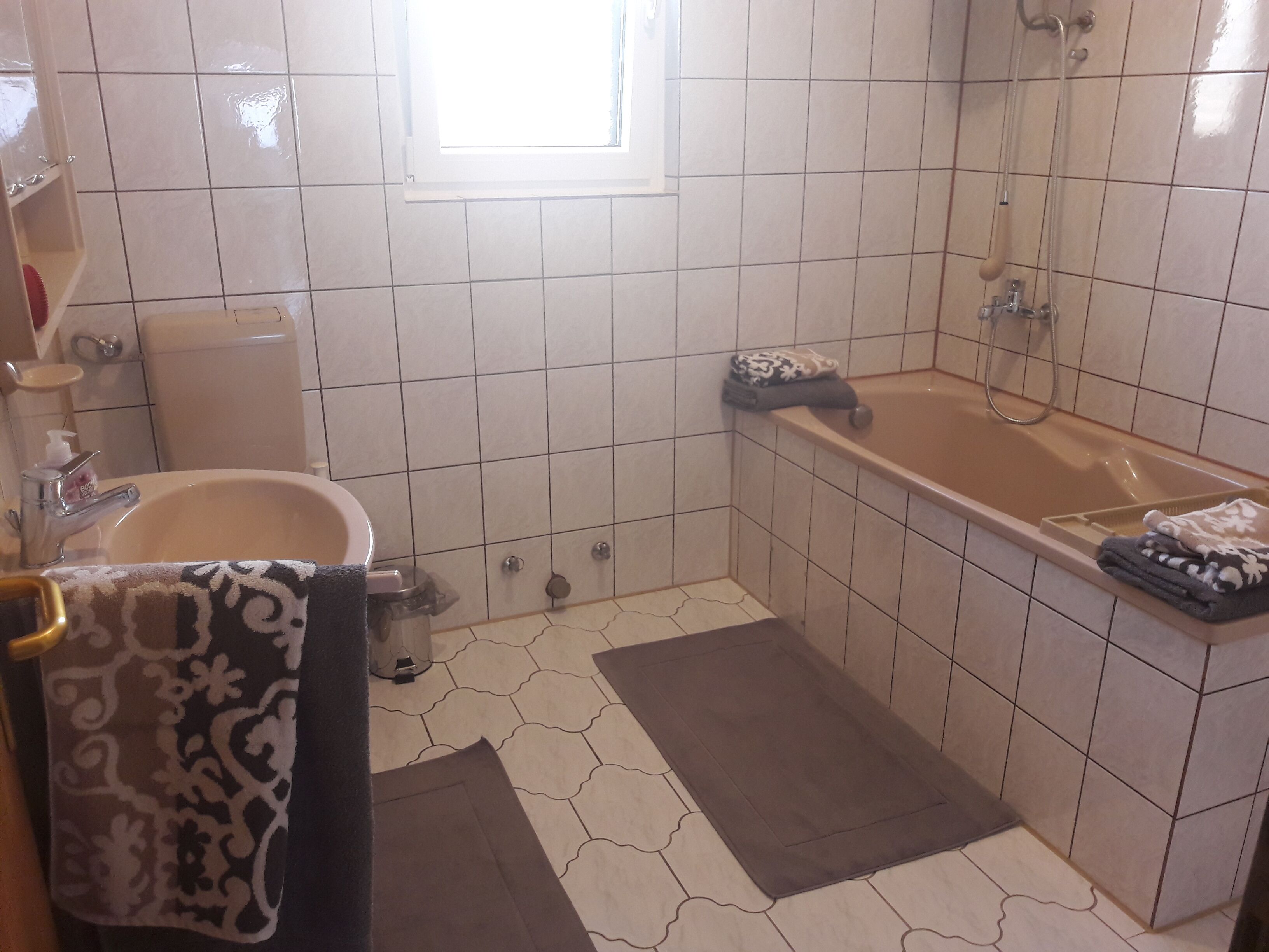 A bathroom with a sink, toilet, and bathtub. There is a window above the sink, and towels are placed on the floor.