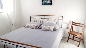 Un dormitorio con una cama, almohadas, una silla, un cuadro y una ventana.