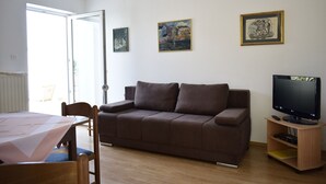 Een woonkamer met een bruine bank, een televisie op een houten dressoir en twee ingelijste kunstwerken aan de muur.