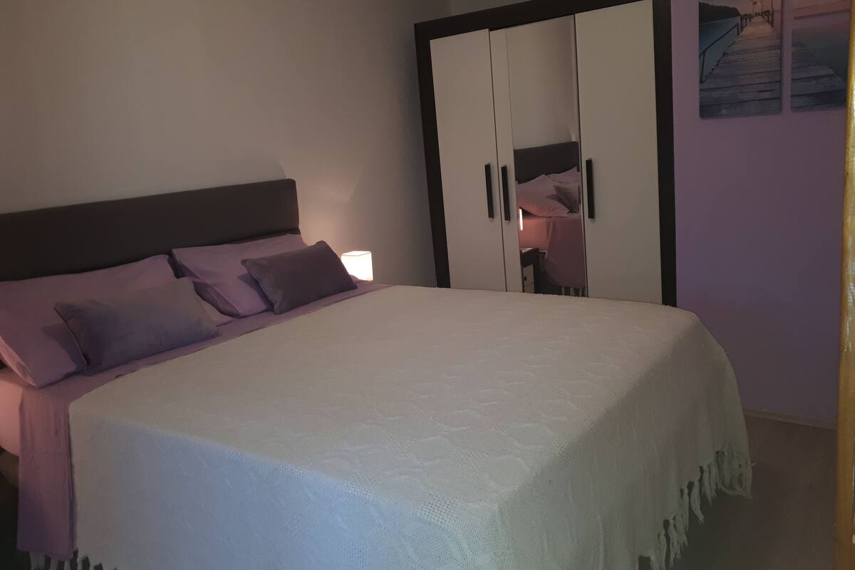 Un dormitorio con cama, almohadas, mesita de noche y armario.