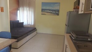 A compact living space with a sofa bed, a dining table, a kitchen area with a sink, and a painting on the wall. - Apartment Sabina & Grapes (Malinska-Dubasnica)